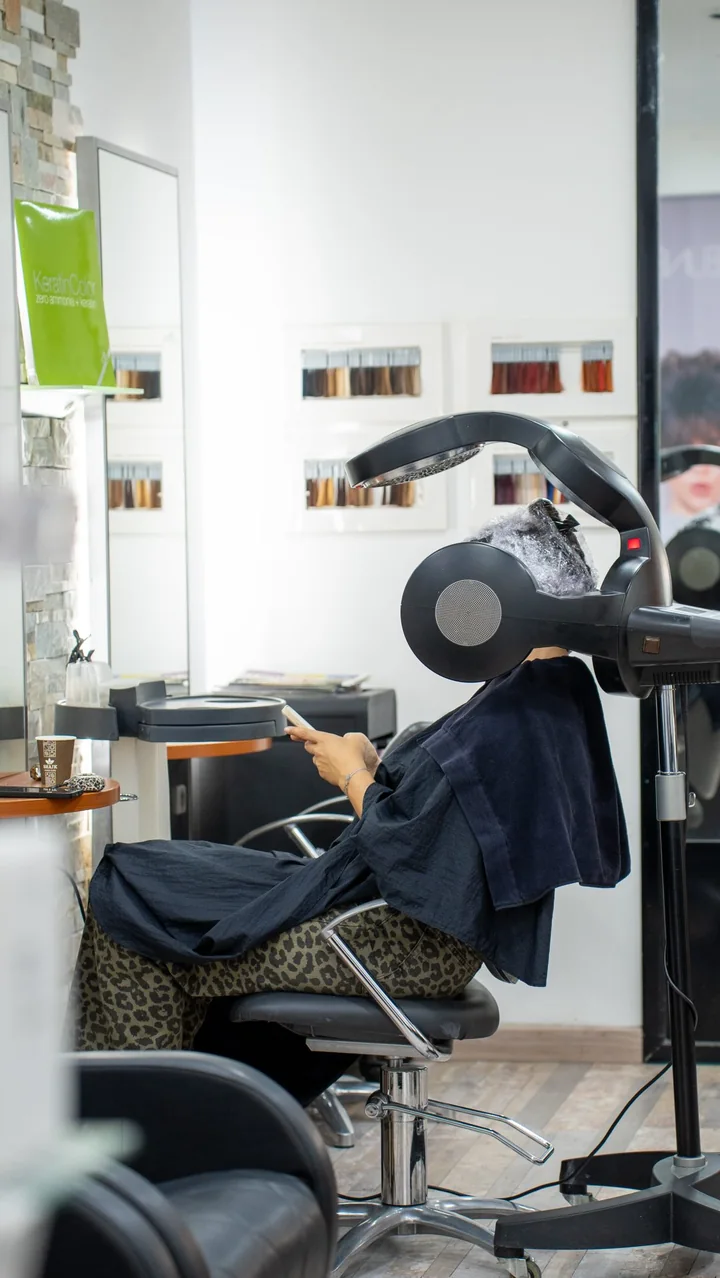 Le salon : une cliente installée sous le casque, nuanciers au mur